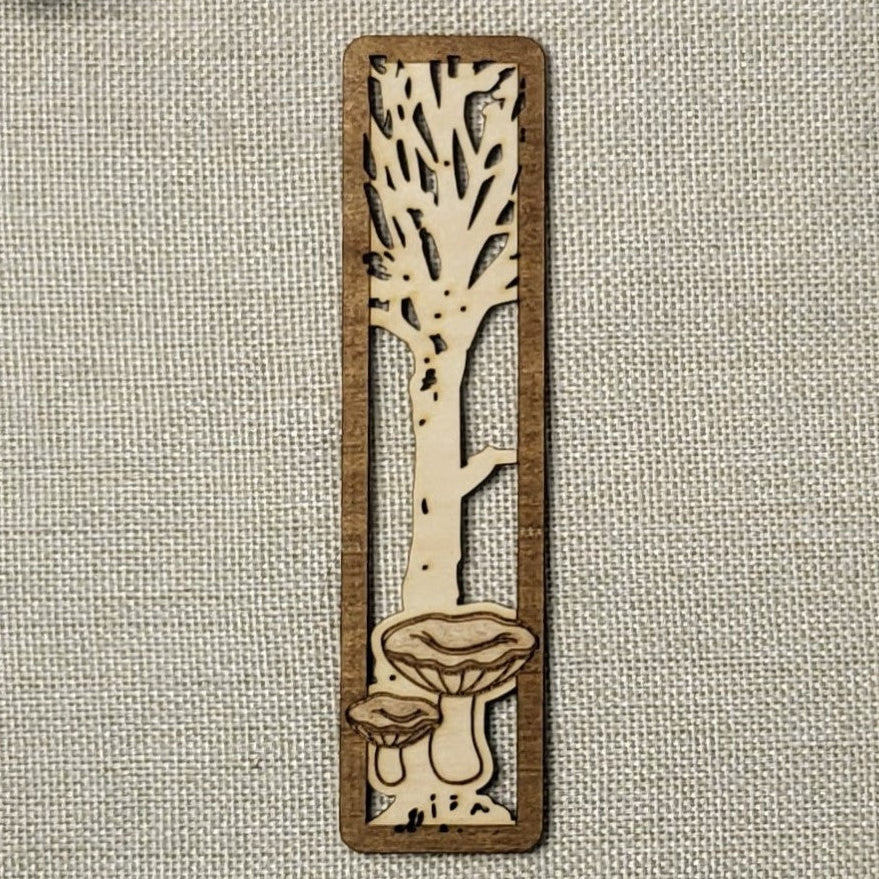 Wooden bookmark with tree and mushroom design on a textured fabric background