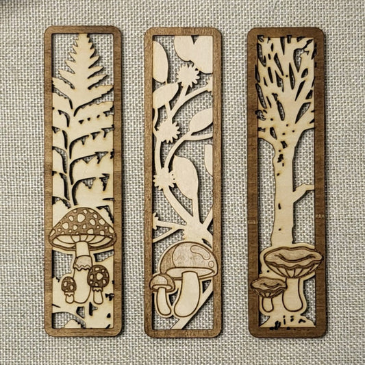 Three wooden bookmarks with laser-cut nature designs on a textured fabric background