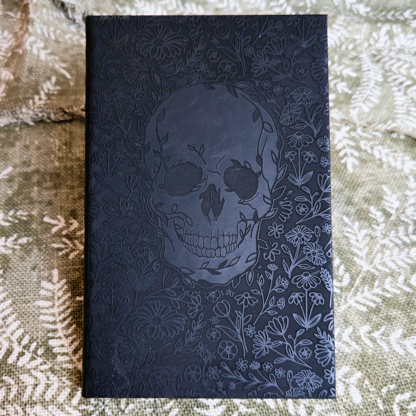 Black notebook with skull and floral design on a textured surface