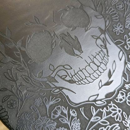 Decorative skull design with floral elements on a leatherette surface